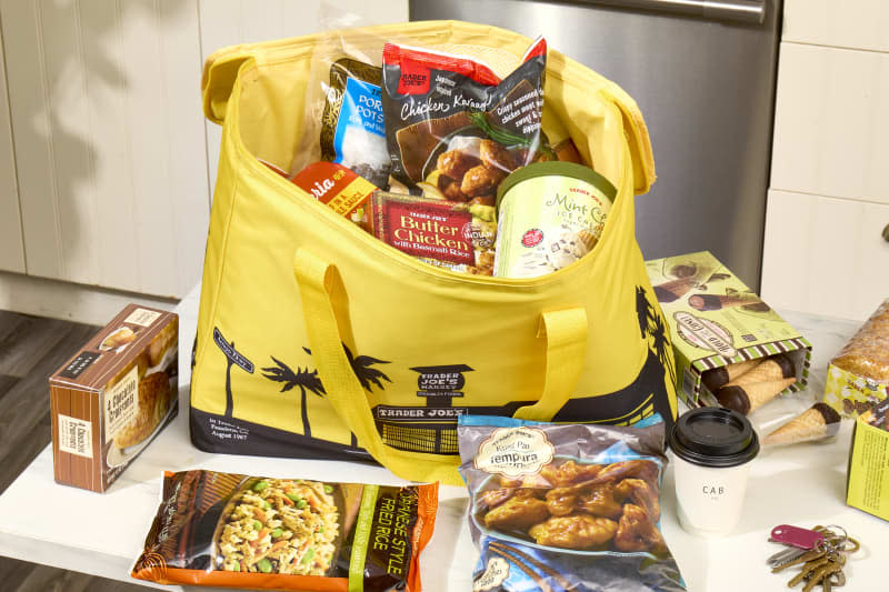 head on shot of an assortment of trader joe's frozen food in a yellow freezer bag, and some scattered on the counter around it.