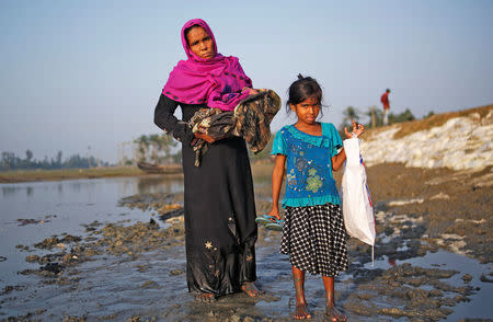 Mobaras Kharun, 40, carrying her newborn baby, and her daughter Shufaida Begum, 6, pose for a picture as they stand in the mud after crossing the Bangladesh-Myanmar border, at a port in Teknaf, Bangladesh October 25, 2017. REUTERS/Adnan Abidi