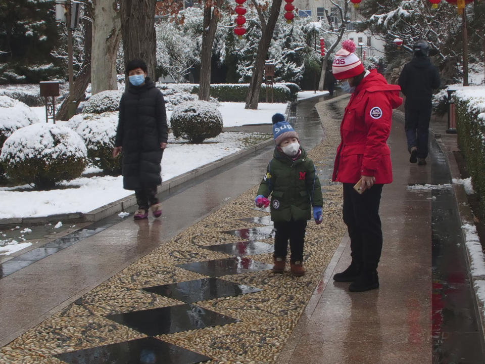 People wear face masks as they walk in public park on a snowy day in Beijing, Sunday, Feb. 2, 2020. The Philippines on Sunday reported the first death from a new virus outside of China, where authorities delayed the opening of schools in the worst-hit province and tightened quarantine measures in a city that allow only one family member to venture out to buy supplies. (Miriam Saleh via AP)