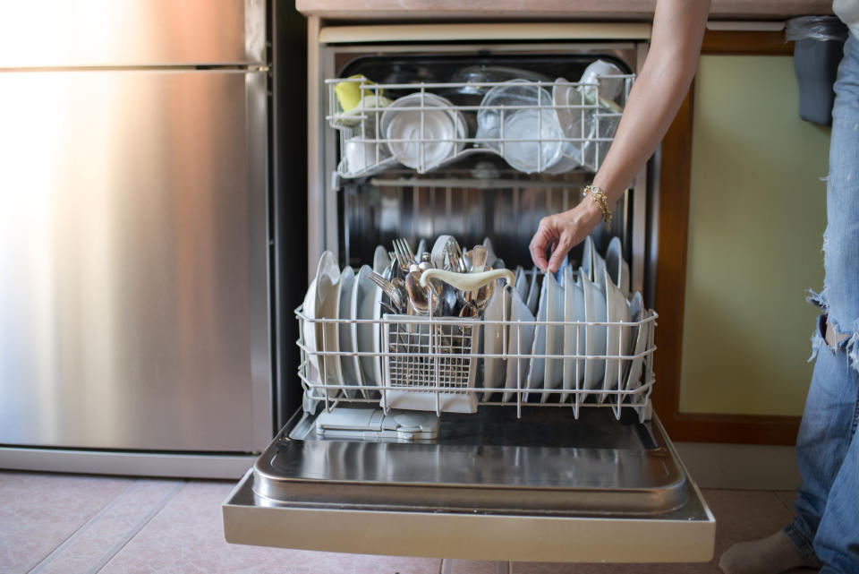 Housewife placing dishes in the dishwasher. Hand or machine dishwashing. Close up shot of modern housewife taking out clean dishes from dishwasher machine.