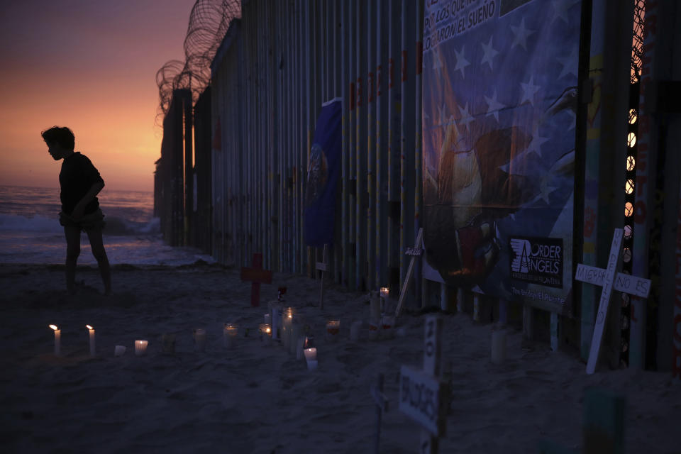 A youth stands by the border fence that separates Mexico from the United States, where candles and crosses stand in memory of migrants who have died during their journey toward the U.S., in Tijuana, Mexico, late Saturday, June 29, 2019. On the border fence at right hangs a cartoon depiction of a news photograph of the bodies of Salvadoran migrant Óscar Alberto Martínez Ramírez and his daughter Valeria, photographed on the banks of the Rio Grande between Matamoros, Mexico, and Brownsville, Texas, after they drowned on Sunday, June 23. (AP Photo/Emilio Espejel)