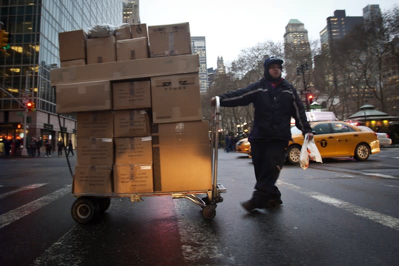 A FedEx delivery person wheels a trolley full of packages across 42nd Street in New York