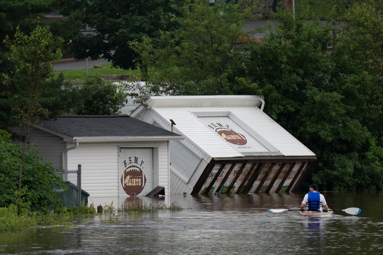 Buildings are seen upended on a riverbank as a man paddles a kayak through floodwater in Bedford, N.S., on July 22. Intense thunderstorms dumped record amounts of rain across a wide swath of Nova Scotia, causing flash flooding, road washouts and power outages.  (The Canadian Press/Darren Calabrese - image credit)