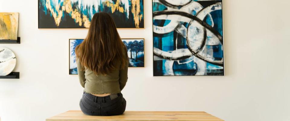 Young female visitor looking reflective while sitting on a bench and admiring the various paintings on the wall of an art gallery