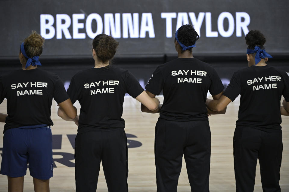 Minnesota Lynx players lock arms with black T-shirts on that say "Say Her Name." 