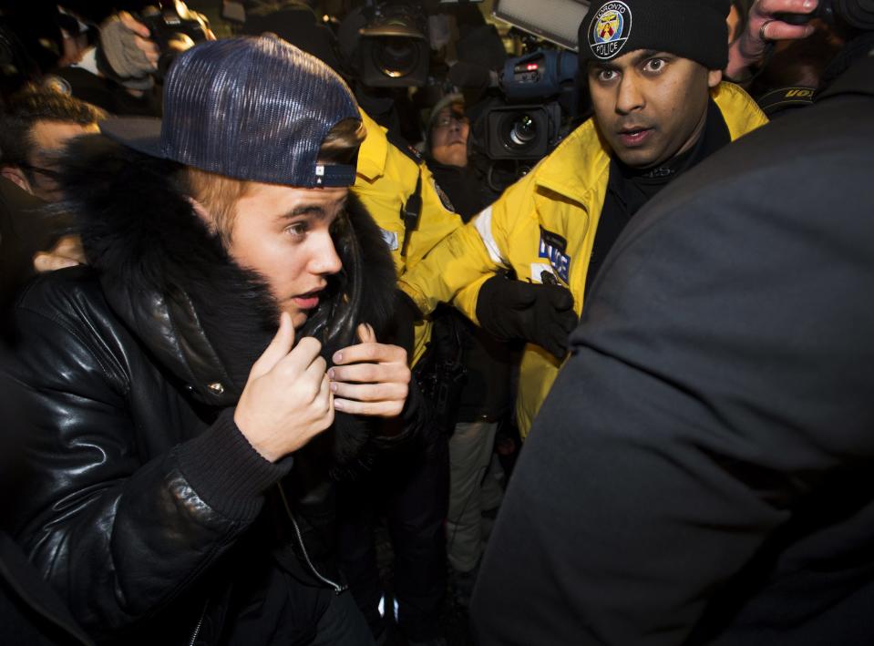 Canadian musician Justin Bieber is swarmed by media and police officers as he turns himself in to city police for an expected assault charge, in Toronto, on Wednesday, Jan. 29, 2014. A police official said the charge has to do with an alleged assault on a limo driver in December. (AP Photo/The Canadian Press, Nathan Denette)