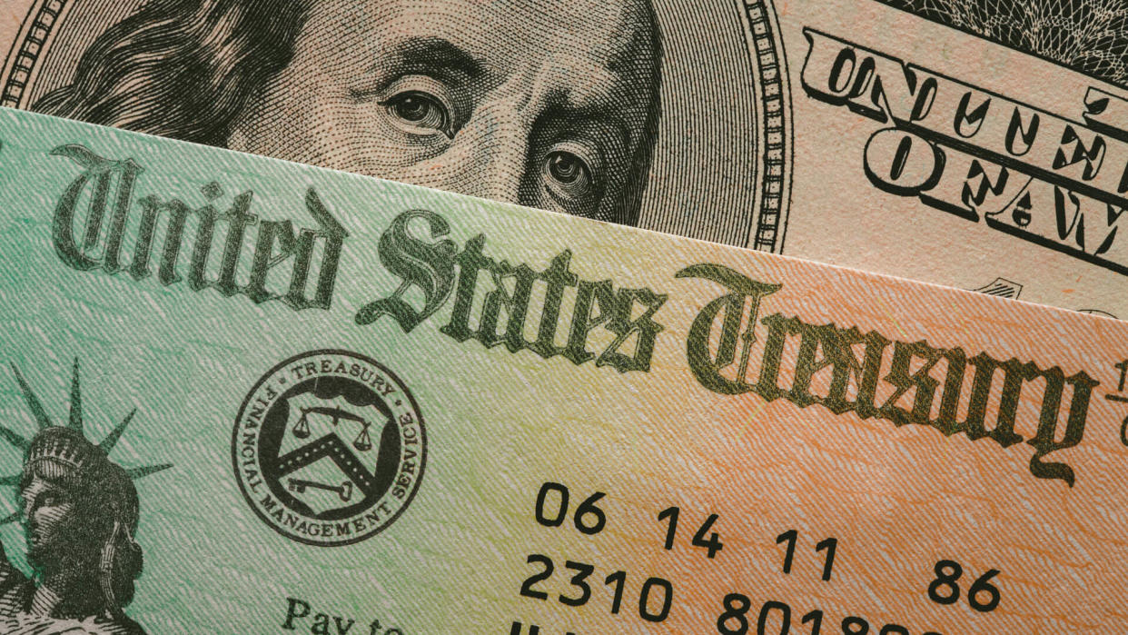 Portrait of Benjamin Franklin on the one hundred dollar bill peering from behind a treasury check issued by the U.S. Government.