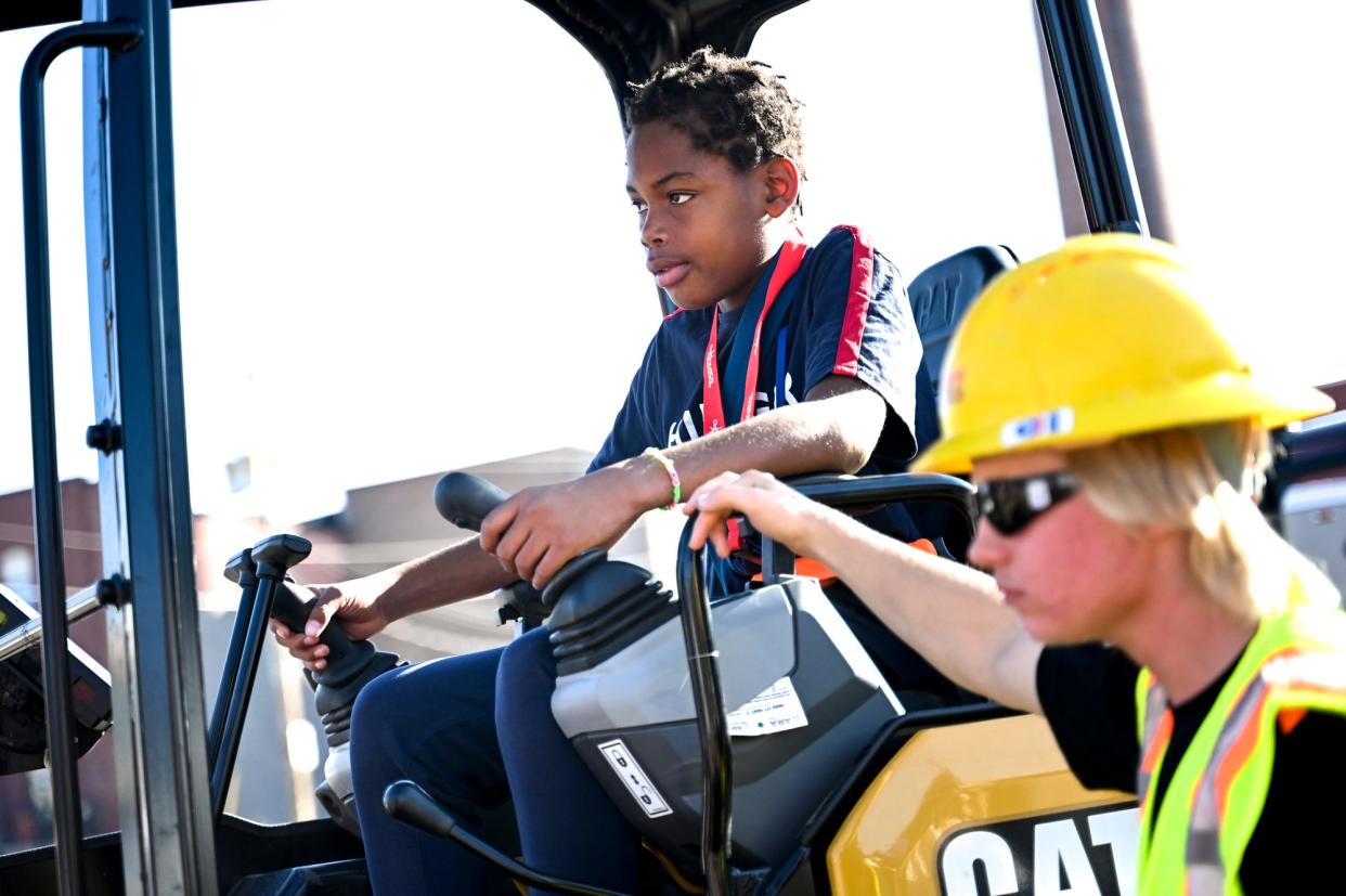 Mt. Hope STEAM School student Davaria Collier, left, uses an excavator to try and place a ball into a 5-gallon bucket as Operating Engineers 324 apprentice Logan Ethington watches during the Construction Science Expo on Tuesday, Oct. 3, 2023, outside Impression 5 Science Center in downtown Lansing.