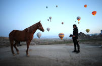 Up, up and away... A man waits patiently with his horse ready to take off with tourists in a hot air balloon in the picturesque region of Cappadocia in Turkey, known for its impressive landscape.