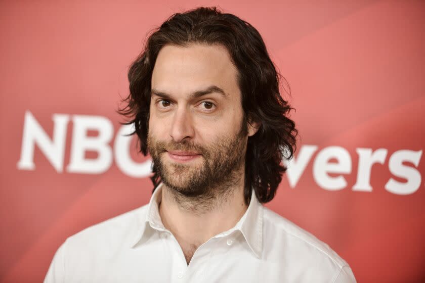 A man with long hair and a beard raises his left eyebrow