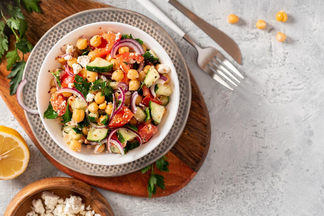 Chickpea salad with tomatoes, cucumber, feta cheese, parsley, onions and lemon in a plate on a gray background top view, selective focus. Healthy vegetarian food, oriental and Mediterranean cuisine.