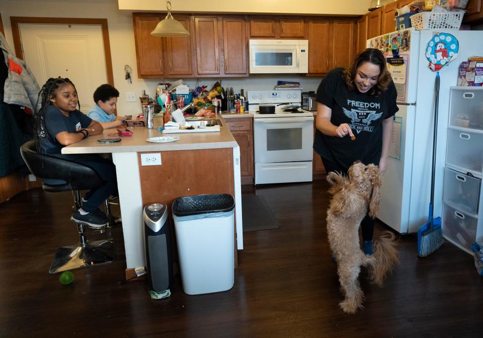 Jasmine Wooten feeds the family dog, Sandie, while her two children, 8-year-old Arius, left, and Naomi, 11, wait for their ramen noodles to be done in their home on the Near East Side. An artist, Wooten recently earned her master's degree in social work from Ohio State University.