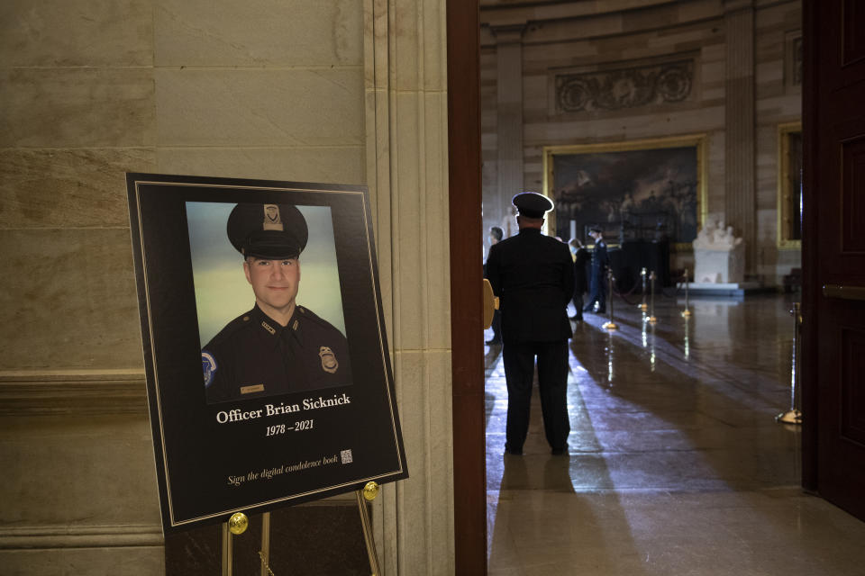 FILE - In this Feb. 2, 2021, file photo a placard is displayed with an image of the late U.S. Capitol Police officer Brian Sicknick on it as people wait for an urn with his cremated remains to be carried into the U.S. Capitol to lie in honor in the Capitol Rotunda in Washington. Federal investigators probing the death Sicknick, a U.S. Capitol Police officer killed in the Jan. 6 riot, have zeroed in on a suspect seen on video appearing to spray a chemical substance on the officer before he later collapsed and died, two people familiar with the matter told The Associated Press. (Brendan Smialowski/Pool via AP, File)