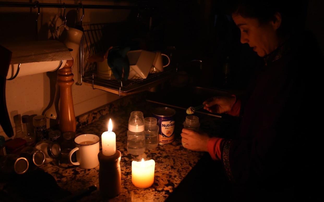 A woman prepares milk bottles using candles at her home in Montevideo  - AFP