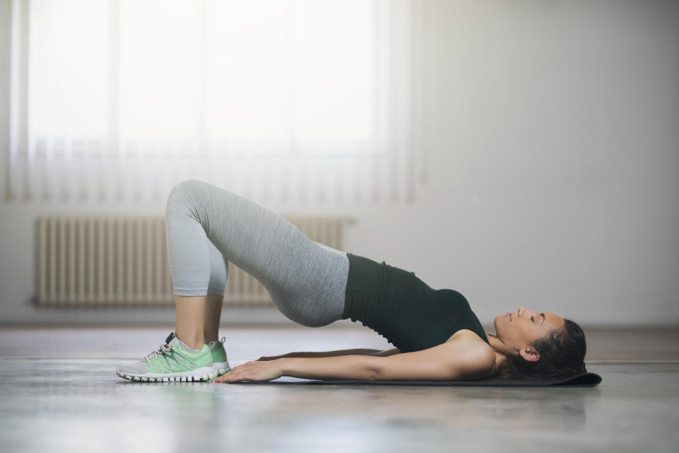 Woman doing a bridge exercise on a mat indoors, wearing a workout outfit of leggings and a tank top