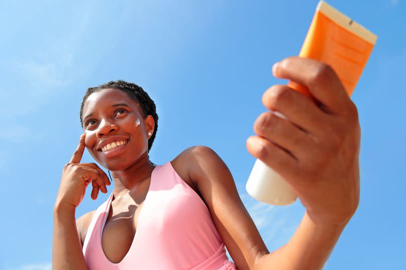 Woman applying sun cream to face with blue sky background