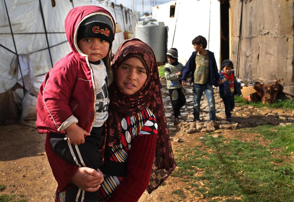 In this picture taken on Wednesday, March 12, 2014, a Syrian girl, foreground, carries her brother walks between tents with other children, background, on their way to a makeshift school at their refugee encampment in the Lebanese-Syrian border town of Majdal Anjar, eastern Bekaa valley, Lebanon. More than 2 million of those who should be in school remain in Syria, where classrooms have been bombed, used as shelters or turned into military barracks. Another 300,000 Syrian children don’t attend school in Lebanon, along with some 93,000 in Jordan, 78,000 in Turkey, 26,000 in Iraq and 4,000 in Egypt, UNICEF officials in Geneva said. Those numbers likely are higher, as UNICEF can’t count the children whose parents didn’t register with the United Nations refugee agency. (AP Photo/Hussein Malla)