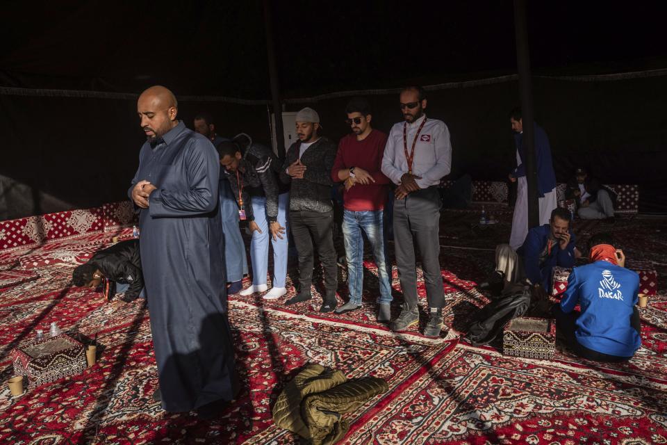 In this Monday, Jan. 13, 2020 photo, Muslims pray at a tent after stage eight of the Dakar Rally in Wadi Al Dawasir, Saudi Arabia. Formerly known as the Paris-Dakar Rally, the race was created by Thierry Sabine after he got lost in the Libyan desert in 1977. Until 2008, the rallies raced across Africa, but threats in Mauritania led organizers to cancel that year's event and move it to South America. It has now shifted to Saudi Arabia. The race started on Jan. 5 with 560 drivers and co-drivers, some on motorbikes, others in cars or in trucks. Only 41 are taking part in the Original category. (AP Photo/Bernat Armangue)