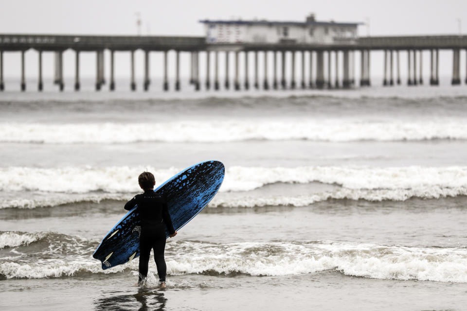 A boy carries a surfboard as he heads towards waves near the Ocean Beach pier Thursday, April 30, 2020, in San Diego. A memo sent to California's police chiefs says Gov. Gavin Newsom intends to close all beaches and state parks starting Friday in the wake of a weekend that saw a crush of people at open seashores. (AP Photo/Gregory Bull)