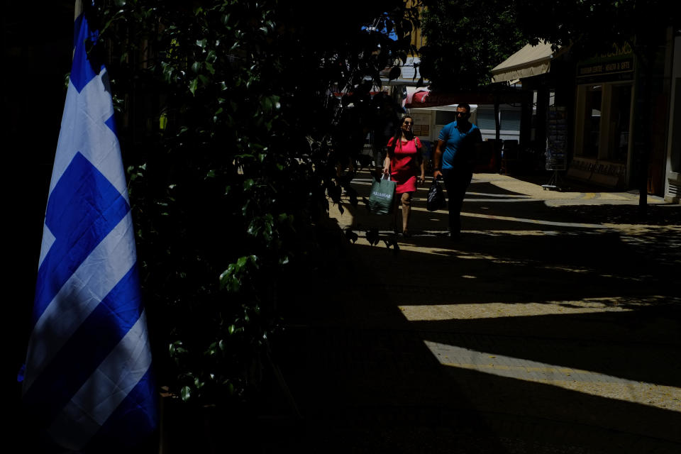 A couple walk on Ledra street a main shopping street as a Greek flag is seen on a Tavern in central Capital Nicosia, Cyprus, Monday, May 25, 2020. Cyprus took a major step toward a return to normality on Thursday when most restrictions of a two month-long stay-at-home order were lifted, allowing primary school kids to return to classes and hair salons and outdoor cafeterias to re-open. (AP Photo/Petros Karadjias)