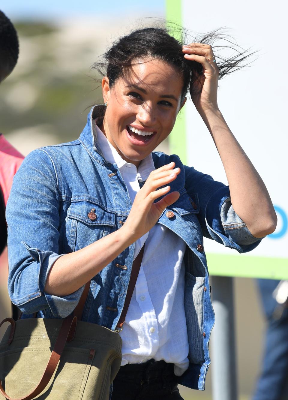 meghan markle in south africa in 2019 wearing a denim jacket and hair blowing in her face