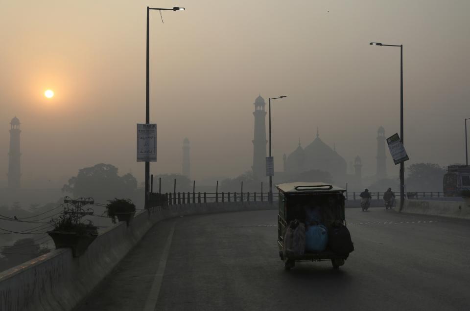 FILE - An auto rickshaw moves on a road as smog envelops the historical Badshahi mosque and the surrounding area of Lahore, Pakistan, Saturday, Nov. 27, 2021. Almost the entire world breathes air that exceeds the World Health Organization's air-quality limits at least occasionally. (AP Photo/K.M. Chaudary, File)