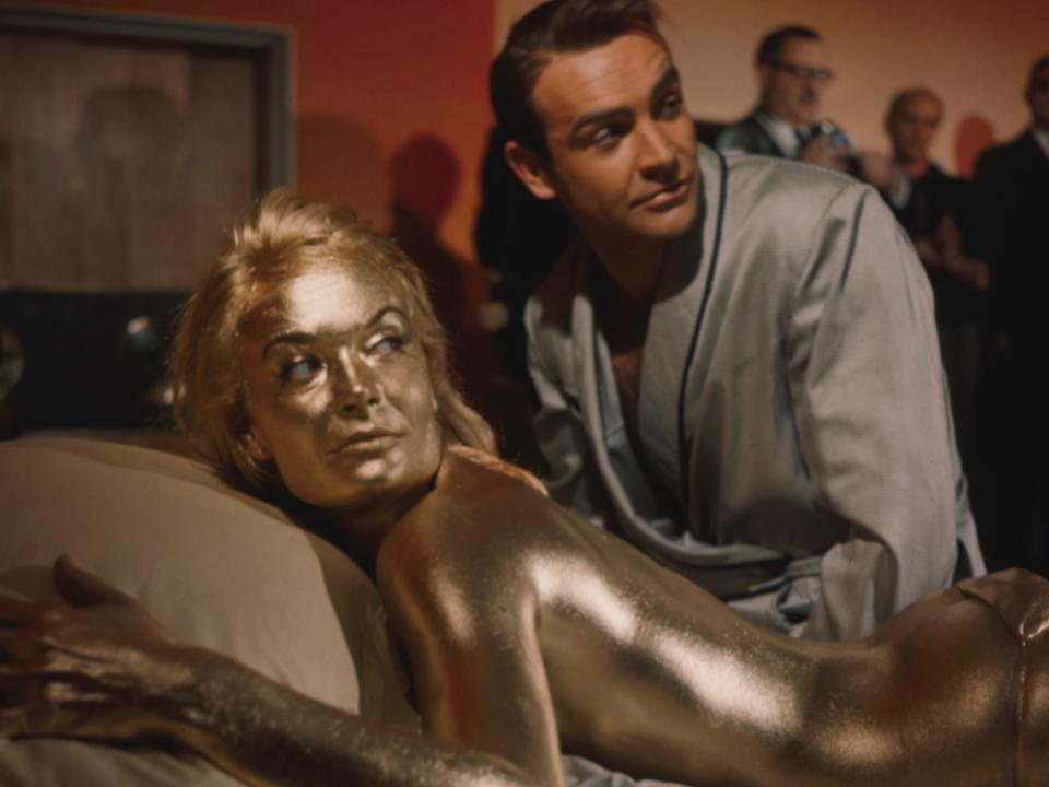 Jill Masterson lying on a bed in gold paint on set of 