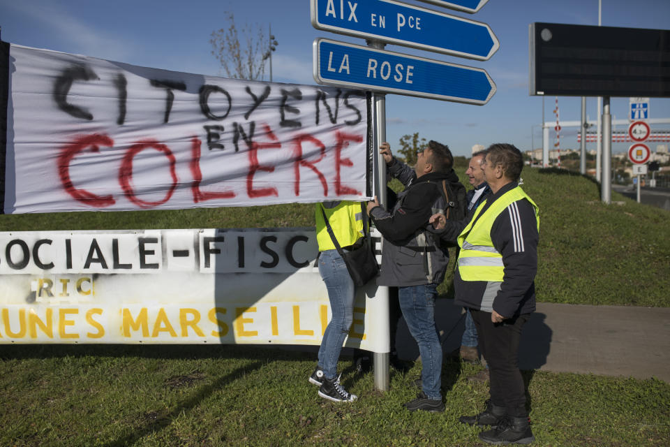 Protesters hang a sign that reads "angry citizens" at a traffic circle during a yellow vest demonstration marking the one year anniversary of the movement in Marseille, southern France, Saturday, Nov. 16, 2019. Police are deployed around key sites in Paris as France's yellow vest protesters prepare to mark the first anniversary of their sometimes-violent movement for economic justice. (AP Photo/Daniel Cole)