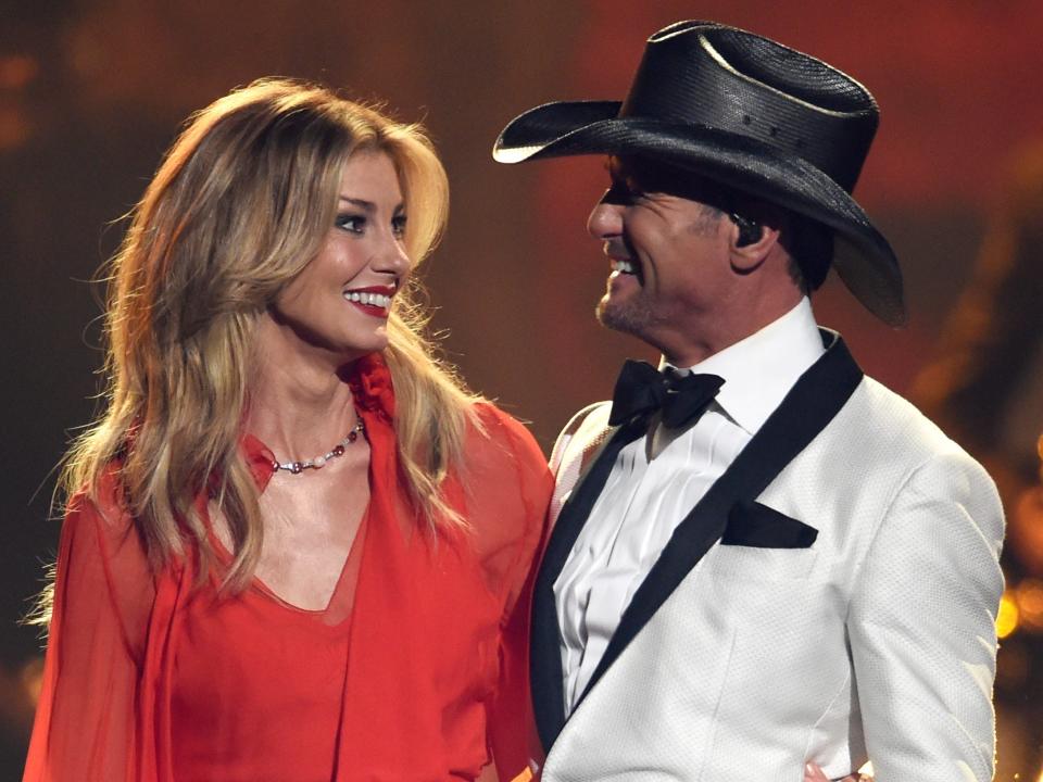 Faith Hill in a red dress and Tim McGraw in a white suit jacket onstage