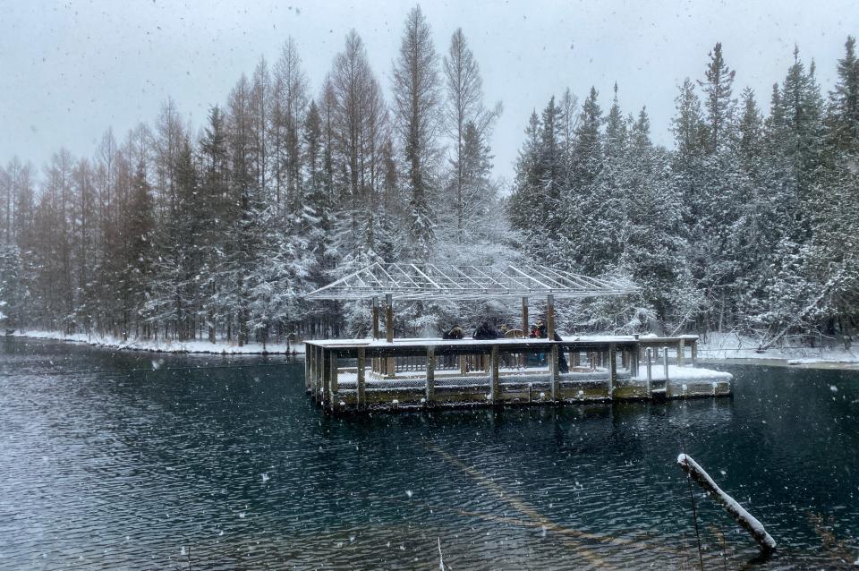 Parkgoers pull themselves across a freshwater spring on a raft using rope system at Kitch-iti-kipi as snow falls at Palms Book State Park in Schoolcraft County in 2023.