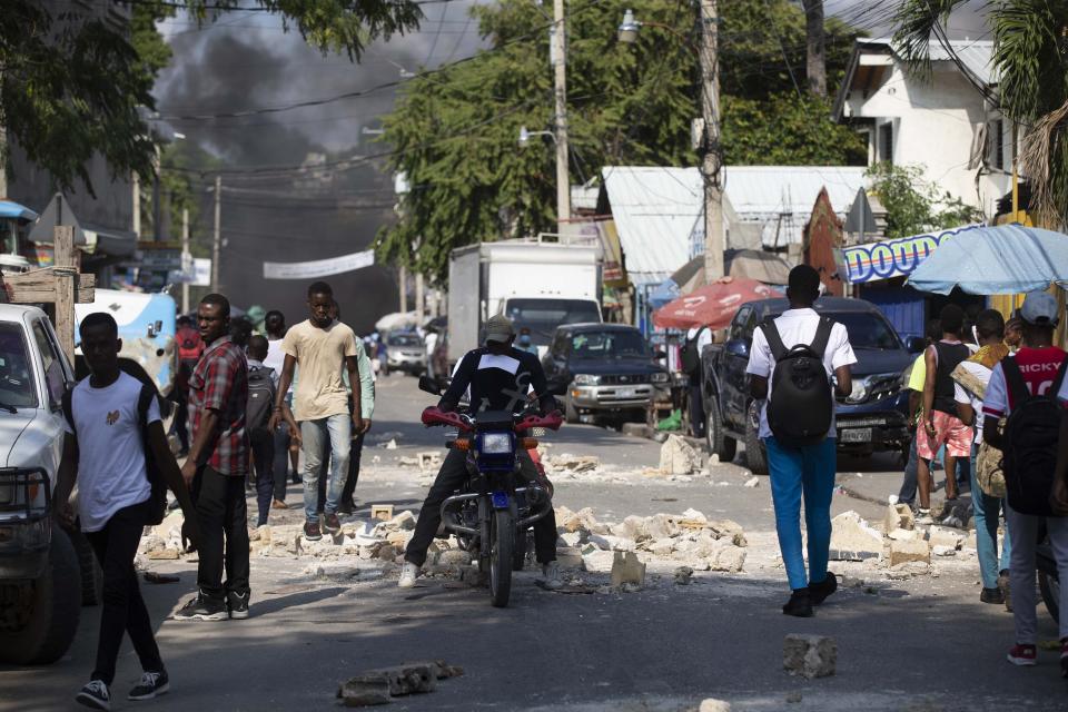 A moto-taxi rides through a barricade of rocks set up by friends and relatives of James Philistin who was kidnapped last night, in Port-au-Prince, Haiti, Wednesday, Nov. 24, 2021. (AP Photo/Odelyn Joseph)