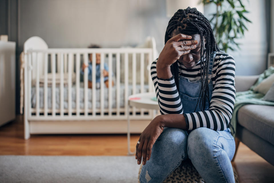 A stressed mother with her baby in a crib behind her