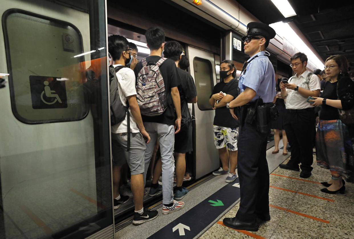 A police officer stands next to some protesters who are blocking the door of a train at a subway platform in Hong Kong on Tuesday, July 30, 2019. Protesters in Hong Kong have disrupted subway service during the morning commute by blocking the doors on trains, preventing them from leaving the stations. (AP Photo/Vincent Yu)