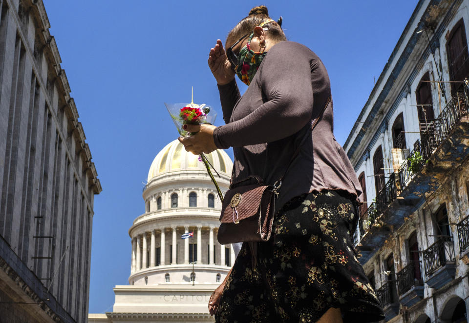 Una mujer, con una mascarilla como protección en medio de la pandemia del coronavirus, se dirige con un pequeño ramo de flores hacia el Teatro Martí para rendir sus últimos respetos a la difunta cantante y actriz cubana Rosita Fornés en un velorio público en La Habana, el martes 16 de junio del 2020. Fornés murió la semana pasada en Miami a los 97 años. Sus restos fueron trasladados a Cuba para su entierro. (AP Foto/Ramón Espinosa)