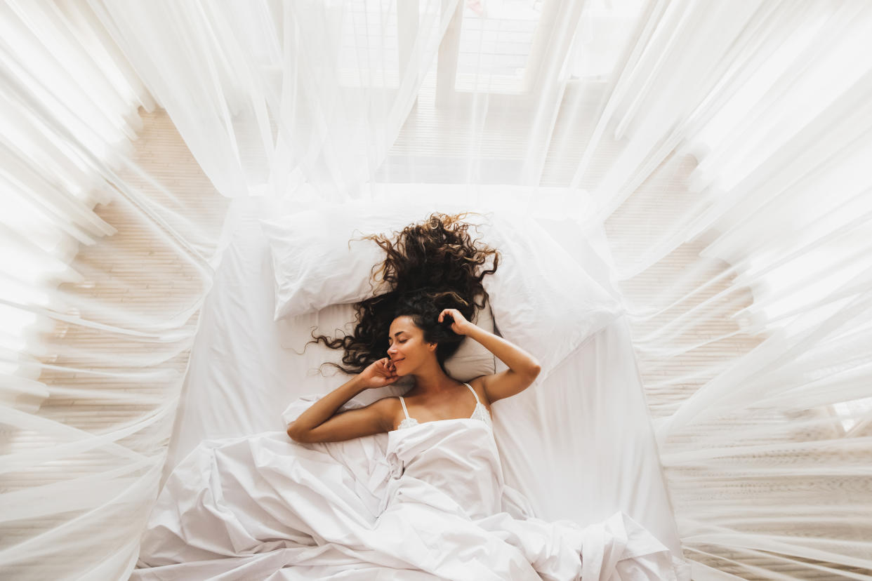 Beautiful smiling girl awakening in white bed. Happy wake up and start new day. Leisure and rest. View from above. Wellbeing concept.