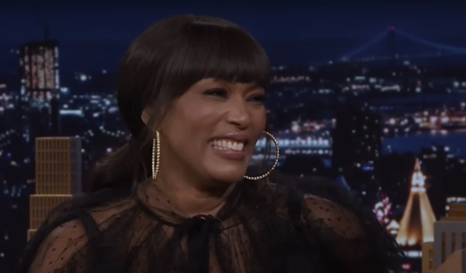 Woman smiling in black attire with sheer details and large hoop earrings on a talk show