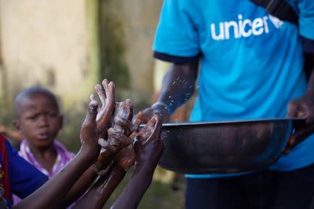 A social mobilizer from NGO Association des Jeunes Conditionnaires et Manutentionnaires (AJCOM), a UNICEF partner, carries a basin of water past the soapy hands of children, to help prevent the spread Ebola in Conakry, Guinea, in this handout photo provided by UNICEF taken September 15, 2014. REUTERS/Timothy La Rose/UNICEF/Handout via Reuters