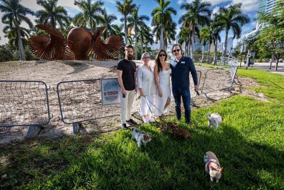 From left to right, Ferre Park regulars Max Méndez and his dog Dominó, Candace O’Brien and her dogs Iris and Ruth, Kelly Sabo with Gigi and TJ Sabo with Stella in the place where one of the oldest trees in Ferre Park was chopped down by the city of Miami without a tree removal permit. An LED billboard is to be erected nearby.