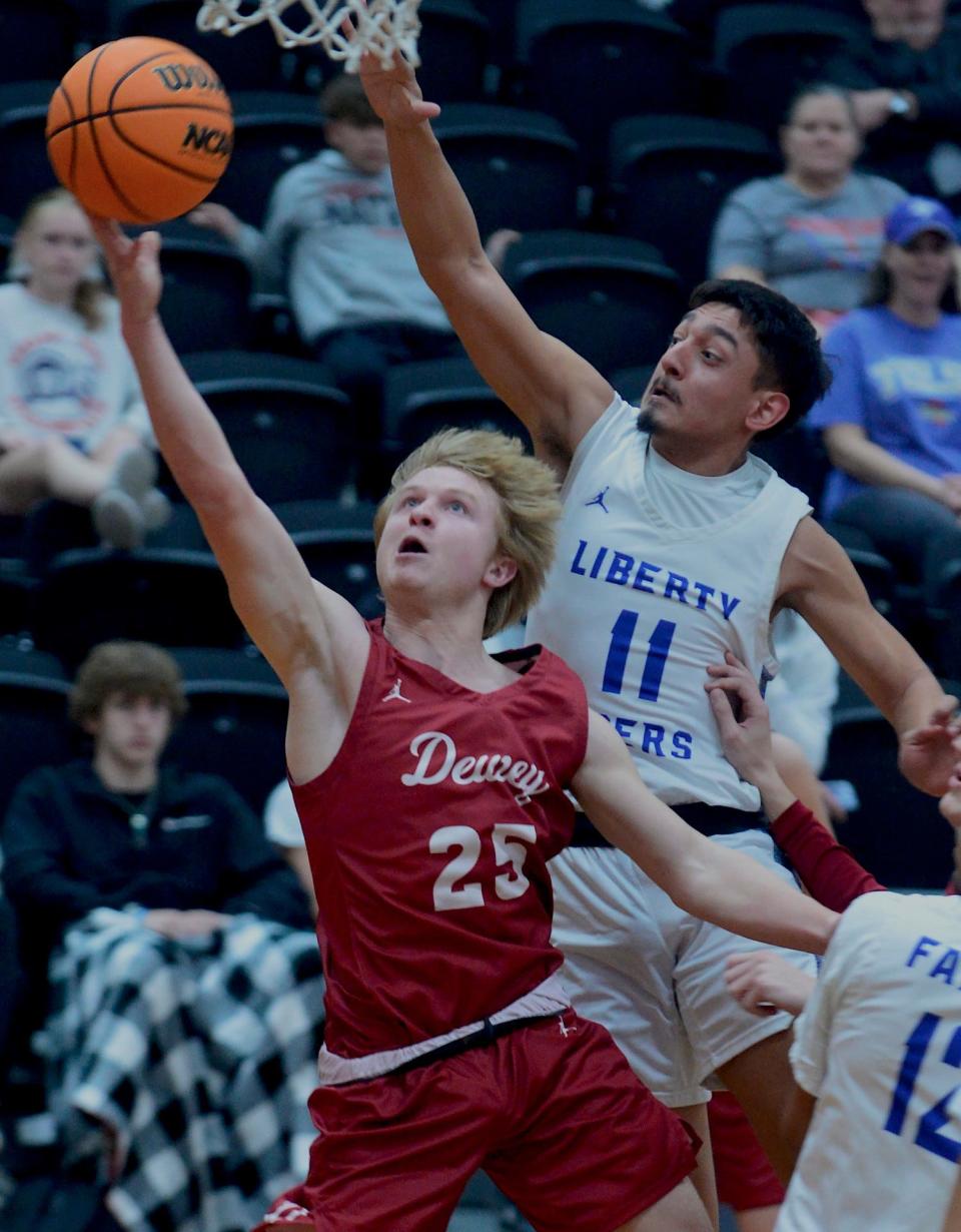 Dewey High School Colby Miller, left, extends toward the rim during boys basketball semifinal play against Liberty High on Jan. 20, 2023, in the Caney Valley Invitational.
