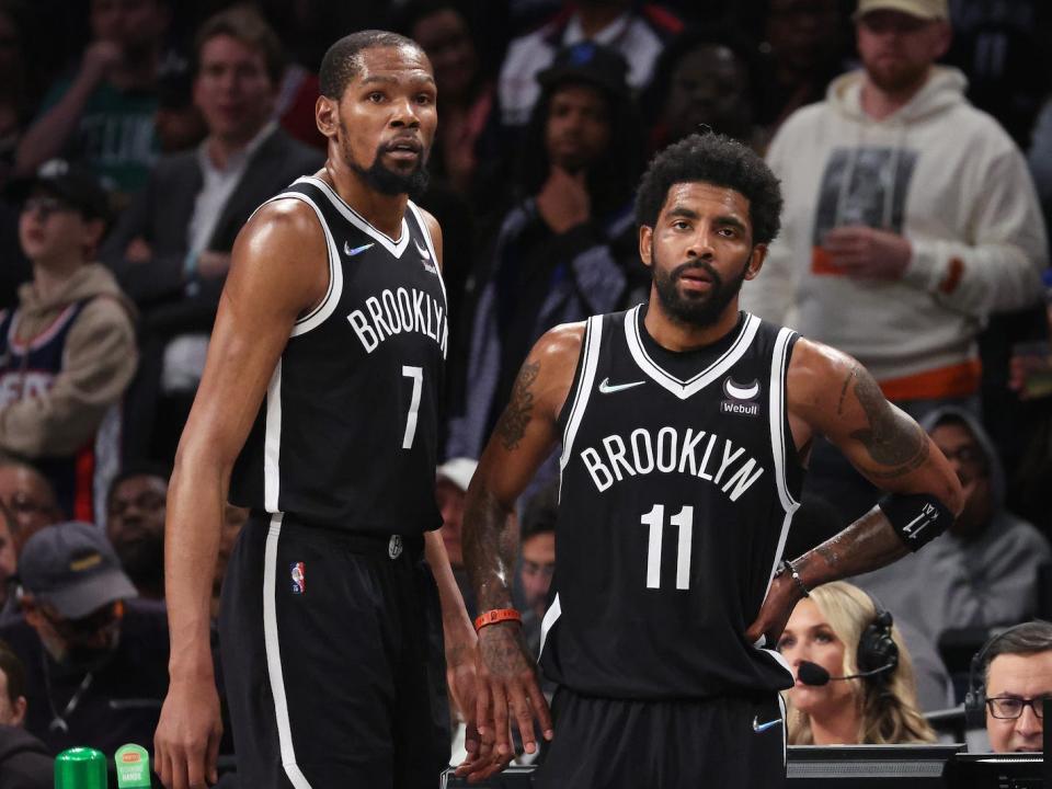 Kevin Durant and Kyrie Irving stand next to one another and look on during a game.