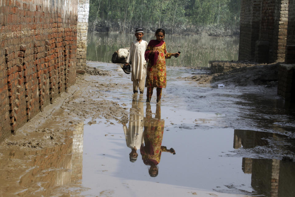 A boy and girl wade through mud near their flood-hit home, in Charsadda, Pakistan, Wednesday, Aug. 31, 2022. Officials in Pakistan raised concerns Wednesday over the spread of waterborne diseases among thousands of flood victims as flood waters from powerful monsoon rains began to recede in many parts of the country. (AP Photo/Mohammad Sajjad)