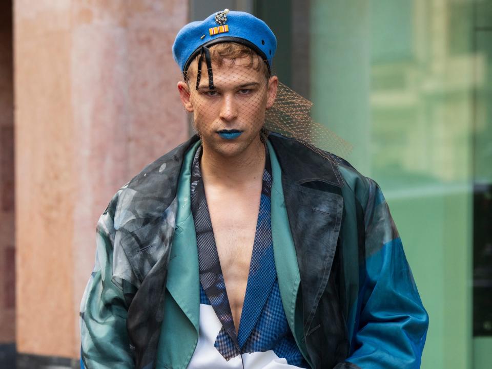 Tommy Dorfman in blue hat, blue lipstick, and blue ensemble