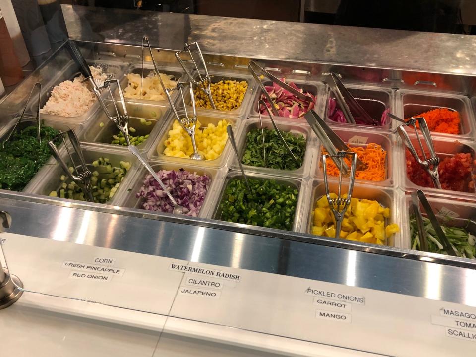 Poke toppings in containers behind the counter at Poke Papa. The options include mango, pineapple, and corn.