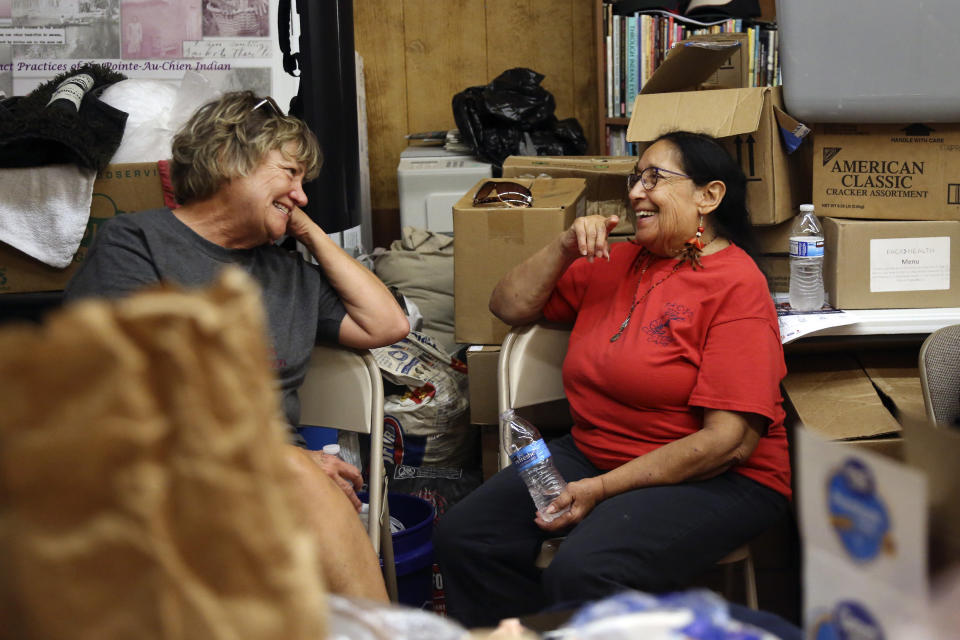 Joy Acosta, left, and Theresa Dardar talk in the Pointe-au-Chien Indian Tribe gathering center, which now doubles as an aid facility stocked with food and supplies for the community in Pointe-aux-Chenes, La., on Tuesday, Sept. 29, 2021, a month after Hurricane Ida made landfall in late August. Over the past decade, Dardar and her husband have partnered with faith and community leaders across the Mississippi River Delta to combat climate change and land loss. These efforts have included initiatives such as building living shorelines, refilling canals dug by oil companies and building an elevated greenhouse to protect medicinal plants and herbs from flooding. (AP Photo/Jessie Wardarski)