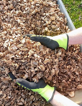 Hands in yellow gloves hold up wood chips.