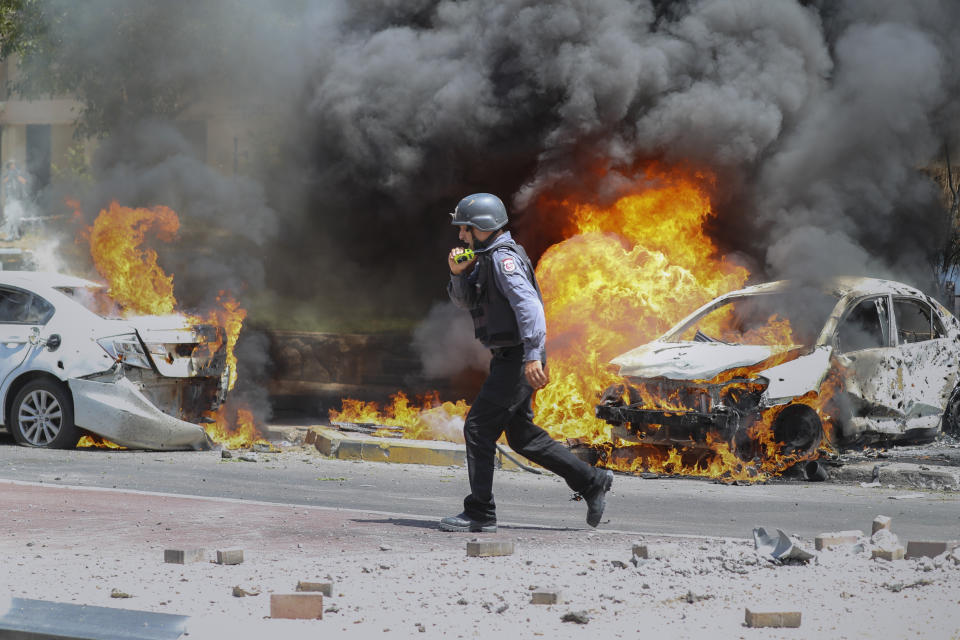 Un bombero israelí camina junto a autos alcanzados por un misil lanzado desde la Franja de Gaza, en la localidad sureña israelí de Ashkelon, el martes 11 de mayo de 2021. (AP Foto/Ariel Schalit)