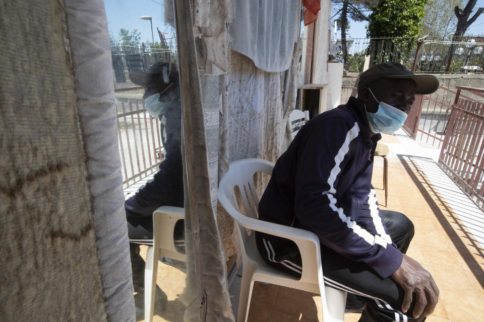 In this photo taken on Monday, April 27, 2020, a man sits outside an house where 46 men, from Nigeria and Ghana live in Castel Volturno, near Naples, Southern Italy. The house has no running water, the dilapidated electrical system doesn't reach many rooms that are in the dark. They are known as “the invisibles,” the undocumented African migrants who, even before the coronavirus outbreak plunged Italy into crisis, barely scraped by as day laborers, prostitutes and seasonal farm hands. Locked down for two months in their overcrowded apartments, their hand-to-mouth existence has grown even more precarious with no work, no food and no hope. (AP Photo/Alessandra Tarantino)