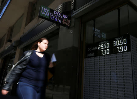 FILE PHOTO: A woman walks past an electronic board showing currency exchange rates, in Buenos Aires' financial district, Argentina August 16, 2018. REUTERS/Agustin Marcarian