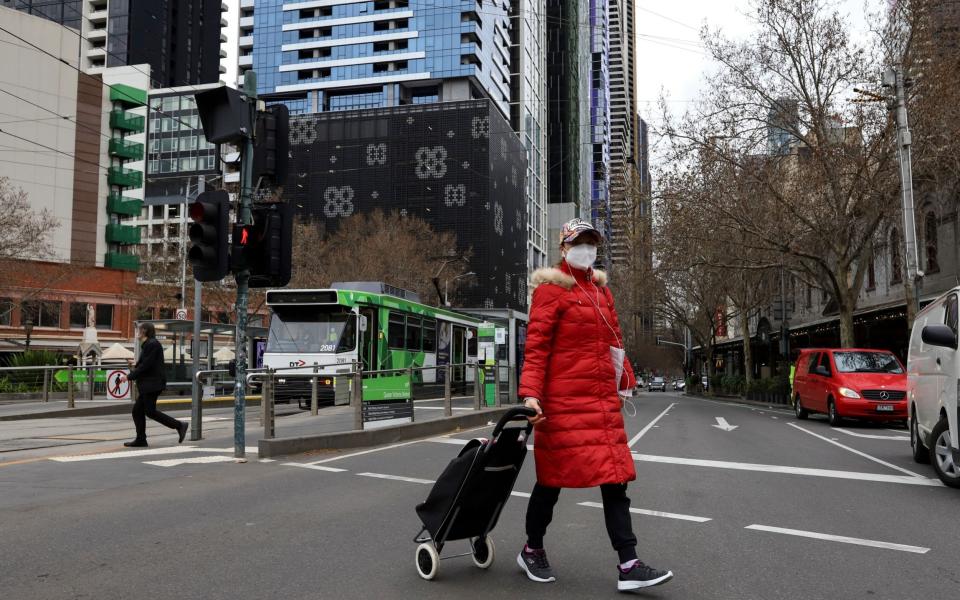 A woman wearing a face mask crosses a street in Melbourne, Victoria, Australia, 06 August 2021. Victoria has entered a seven-day lockdown in an effort to contain a growing outbreak of the COVID-19 Delta variant in the state. COVID-19 lockdown in Melbourne, Australia - Shutterstock