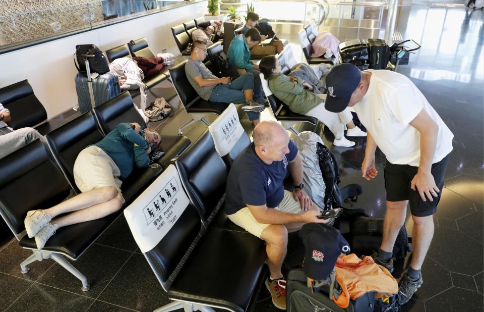 Passengers, including a British man who came for the Rugby World Cup, rest and wait for their flights which were cancelled because of Typhoon Hagibis, at Haneda Airport in Tokyo, Saturday, Oct. 12, 2019. Tokyo and surrounding areas braced for a powerful typhoon forecast as the worst in six decades, with streets and trains stations unusually quiet Saturday as rain poured over the city. (Kyodo News via AP)